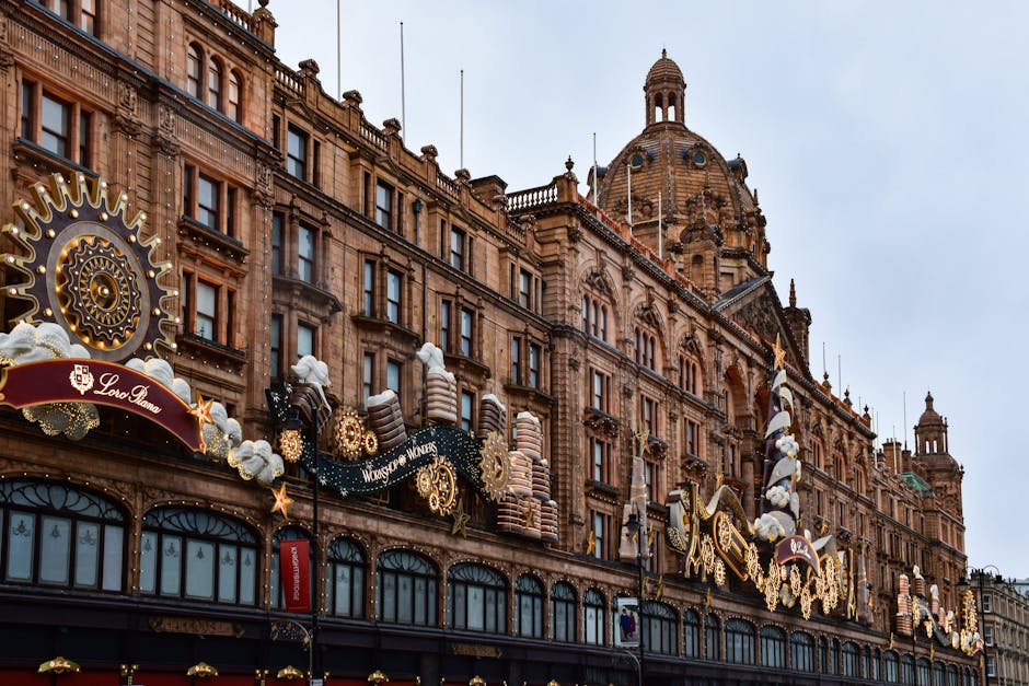 The exterior of a historic building in Knightsbridge decorated for the holiday season with large ornate gingerbread man and star ornaments, golden gears, snowflakes, and festive banners hanging along the facade. The building features a detailed stone facade with tall windows, a central domed tower, and decorative architectural elements. The scene is illuminated by soft natural daylight, highlighting the cleanliness and decorative details of the display, with no visible dirt or clutter. This image showcases the grandeur of the Harrods shopping destination, emphasizing its architectural beauty and seasonal decorations, as seen on the webpage of Cleaner Knightsbridge offering surface cleaning and deep cleaning services in the area.